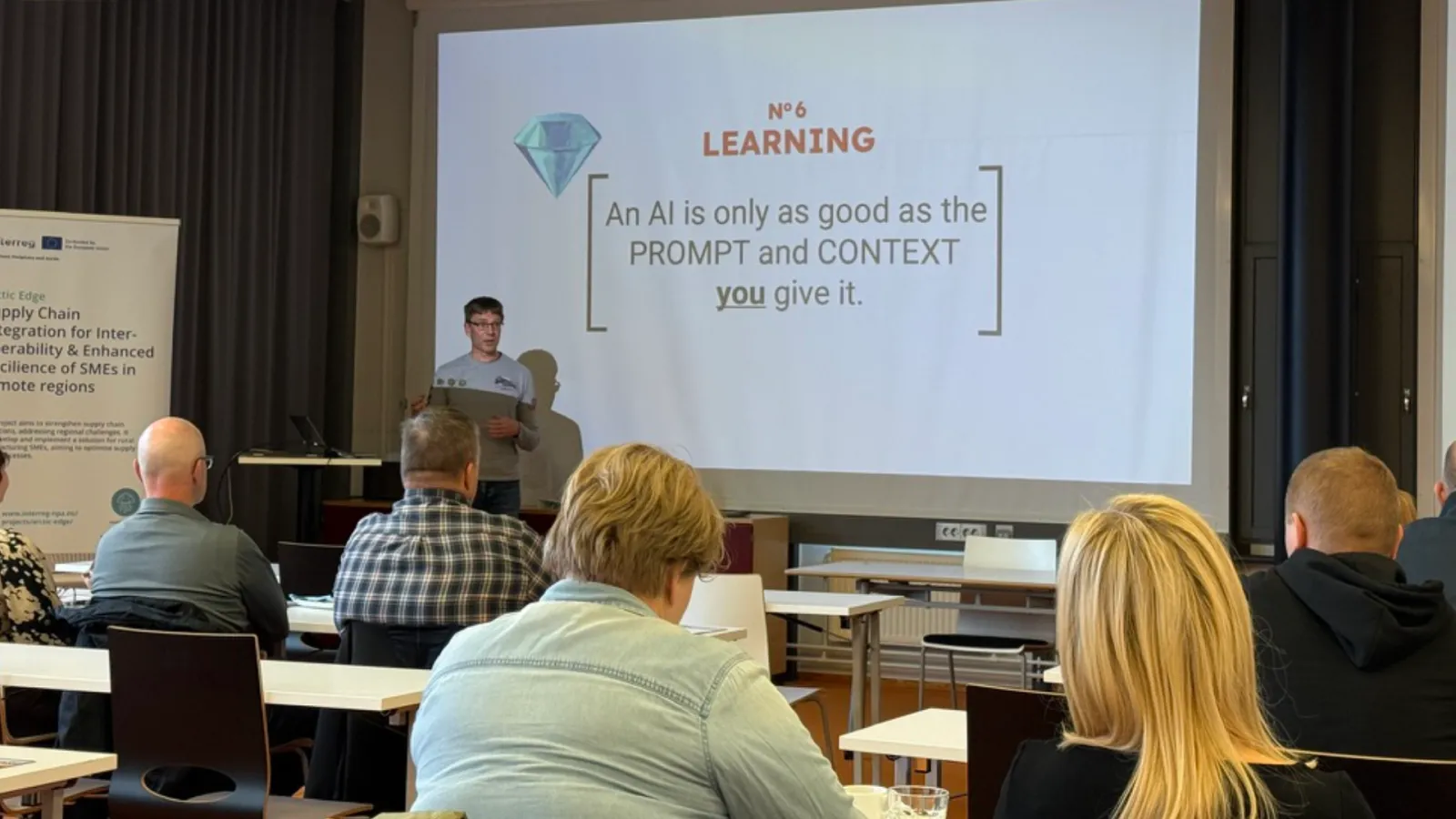 Teemu Piirainen speaking about AI adoption at the North Karelia Chamber of Commerce Digiklinikka event, beside a slide reading 'An AI is only as good as the prompt and context you give it.'